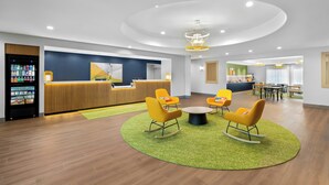 A modern lobby with a reception desk, yellow rocking chairs, a round table, and a vending machine. - Spark by Hilton Missouri City (Missouri City)
