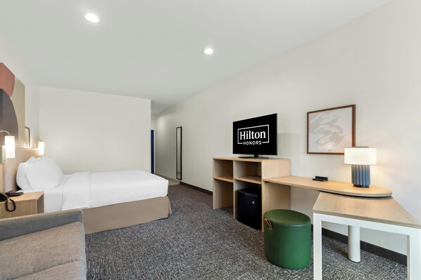 Ein Hotelzimmer mit einem Bett, einem Schreibtisch, einem Fernseher und einer grünen Mülleimer.