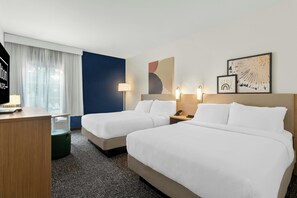 A hotel room with two beds, a desk, a chair, a lamp, and artwork on the wall. - Spark by Hilton Missouri City (Missouri City)
