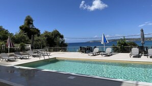 A poolside area with lounge chairs and umbrellas, overlooking a body of water and a distant island. - Agios Gerasimos (Kefalonia)