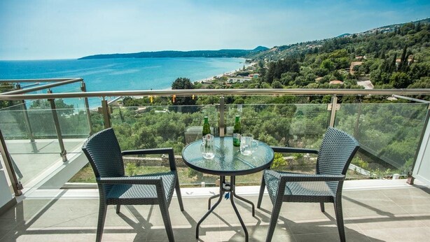 A balcony with a glass table and chairs, overlooking a coastal landscape. - Agios Gerasimos (Kefalonia)