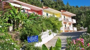 A multi-story building with balconies, surrounded by greenery and a clear sky. - Agios Gerasimos (Kefalonia)