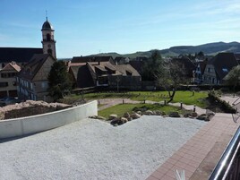 Un pueblo rural con casas tradicionales, una torre de iglesia y un área pavimentada con rocas y un camino.