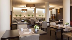 A spacious hotel dining area with multiple tables and chairs, large pendant lights, and potted plants. - Val-vignes Haut-koenigsbourg, The Originals Relais (Saint-Hippolyte)