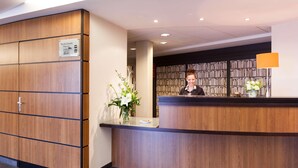 A reception desk with a wooden finish, a sign indicating a restaurant and a bar, and a bookshelf filled with books in the background. - Val-vignes Haut-koenigsbourg, The Originals Relais (Saint-Hippolyte)