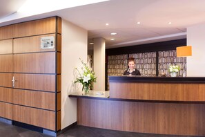 Un comptoir d’accueil avec un revêtement en bois, une enseigne indiquant la présence d’un restaurant et d’un bar, et une bibliothèque remplie de livres en arrière-plan.