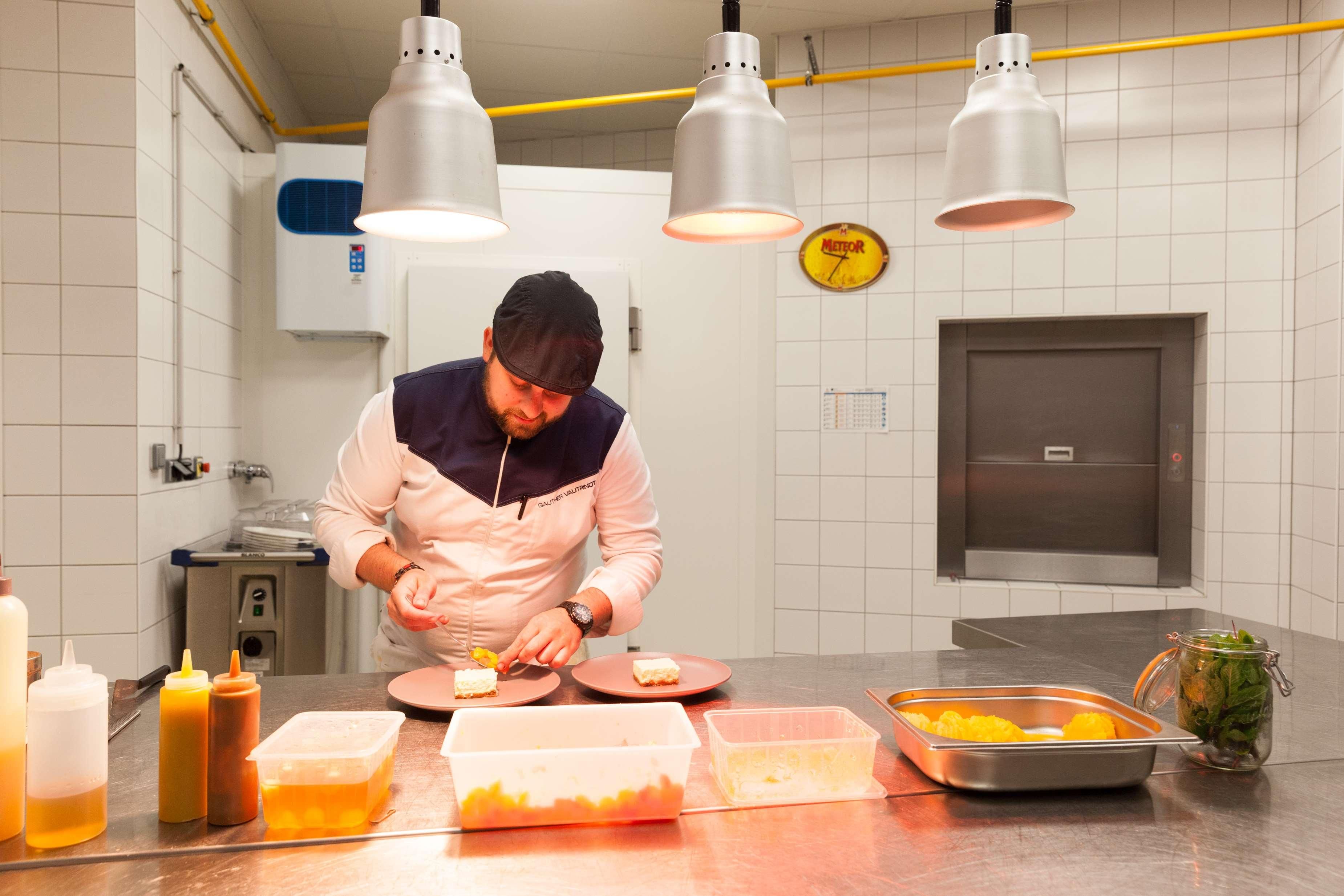 Un chef preparando comida en una cocina moderna con electrodomésticos de acero inoxidable, un reloj e iluminación colgante.