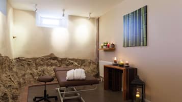 A spa room with a massage table, a small shelf with candles, and a wall-mounted artwork.