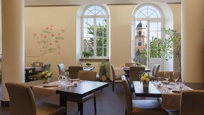 A dining area with tables set for two, large arched windows, and a mural of flowers on the wall. - Val-vignes Haut-koenigsbourg, The Originals Relais (Saint-Hippolyte)