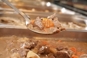 Uma colherada de ensopado com pedaços de carne e cenouras.
