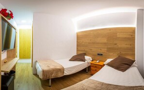 Una habitación de hotel compacta con dos camas individuales, un cabecero de madera, un escritorio pequeño y un televisor.