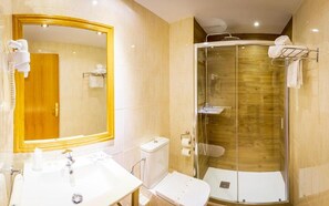 Un baño con un espejo grande, un lavamanos, un inodoro y una ducha con paredes de vidrio.