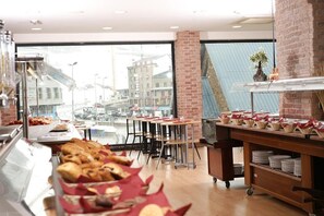 Zona de bufé con mostradores de comida, mesas y vistas a la ciudad a través de amplias ventanas.