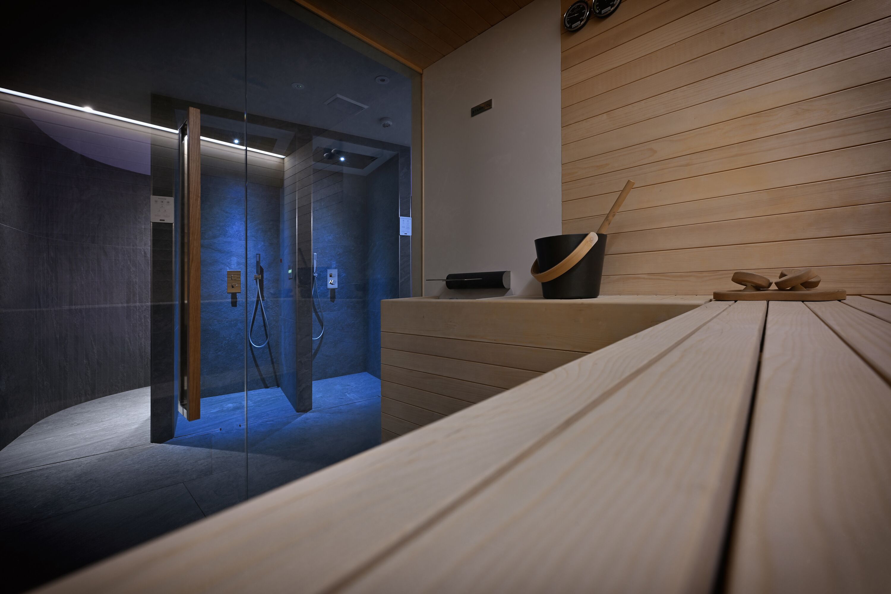 Une salle de spa moderne dotée d’une douche à parois de verre, de lambris en bois et d’un banc en bois.