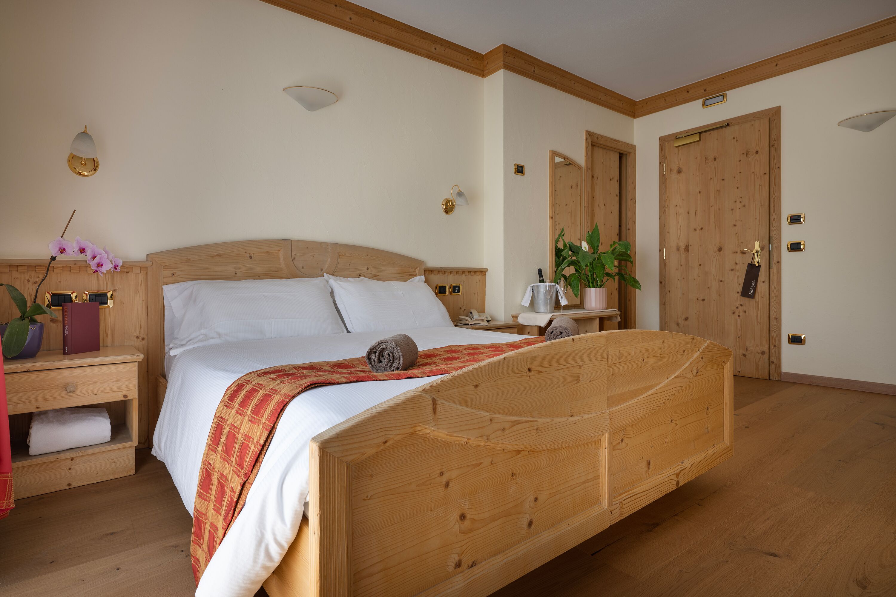 Un lit en bois avec une tête de lit, une table de chevet avec une lampe, une commode et une plante en pot.