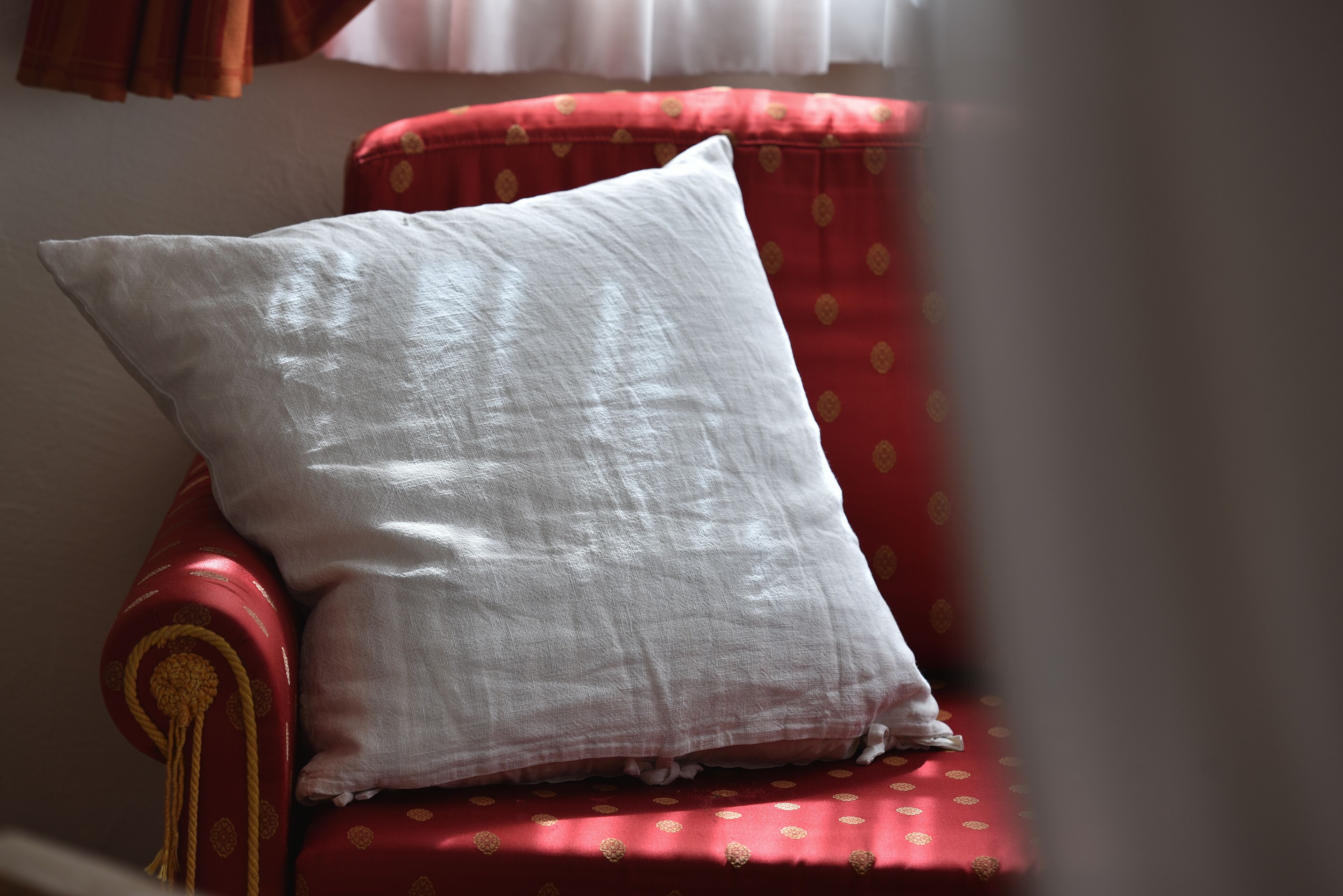 A red armchair with a white pillow and a red cushion with gold patterns.