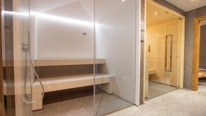 Un baño moderno con ducha envuelta en vidrio, un banco y una puerta de madera que da acceso a la zona de la ducha.