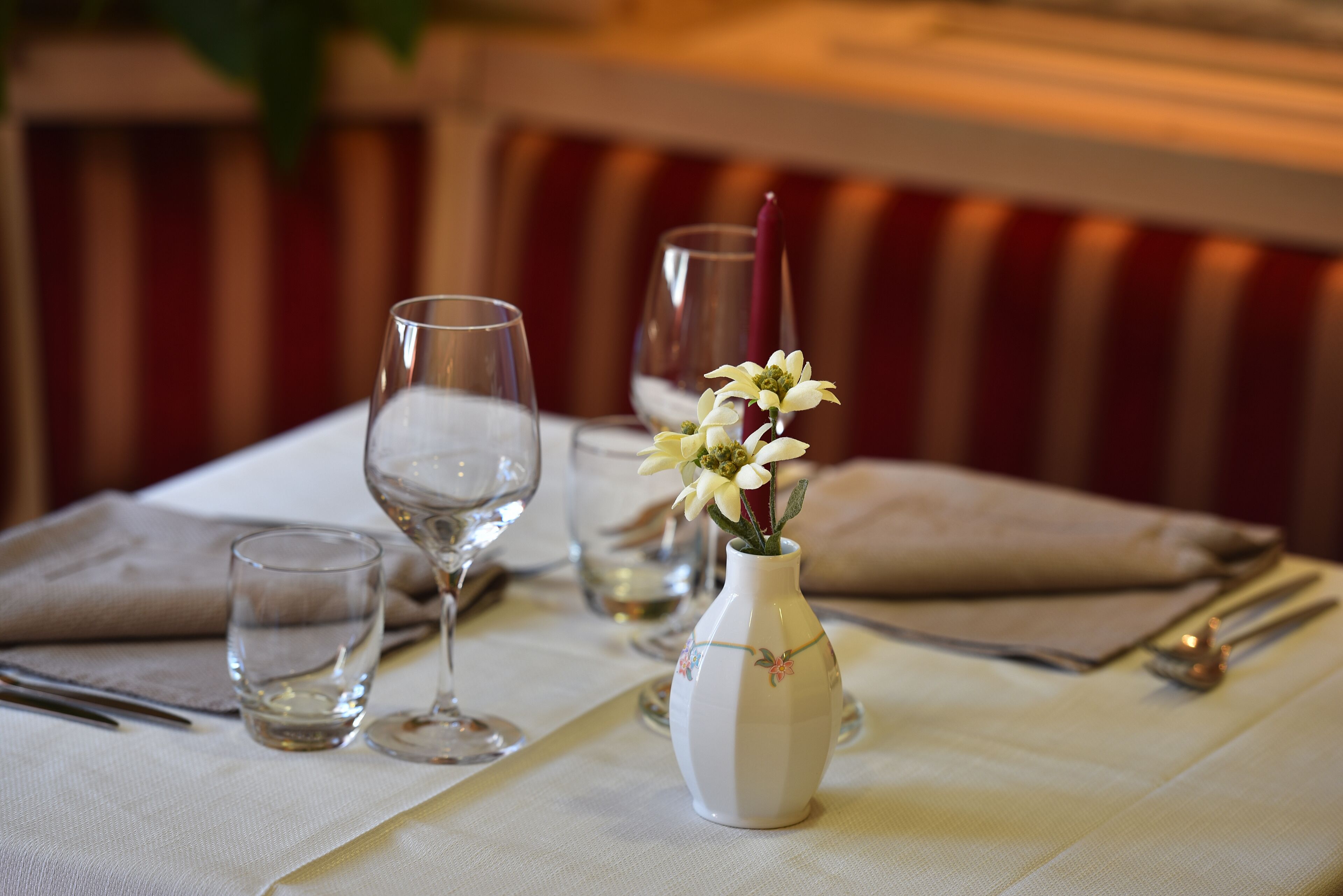 A dining table set with wine glasses, a vase with flowers, and a red candle.