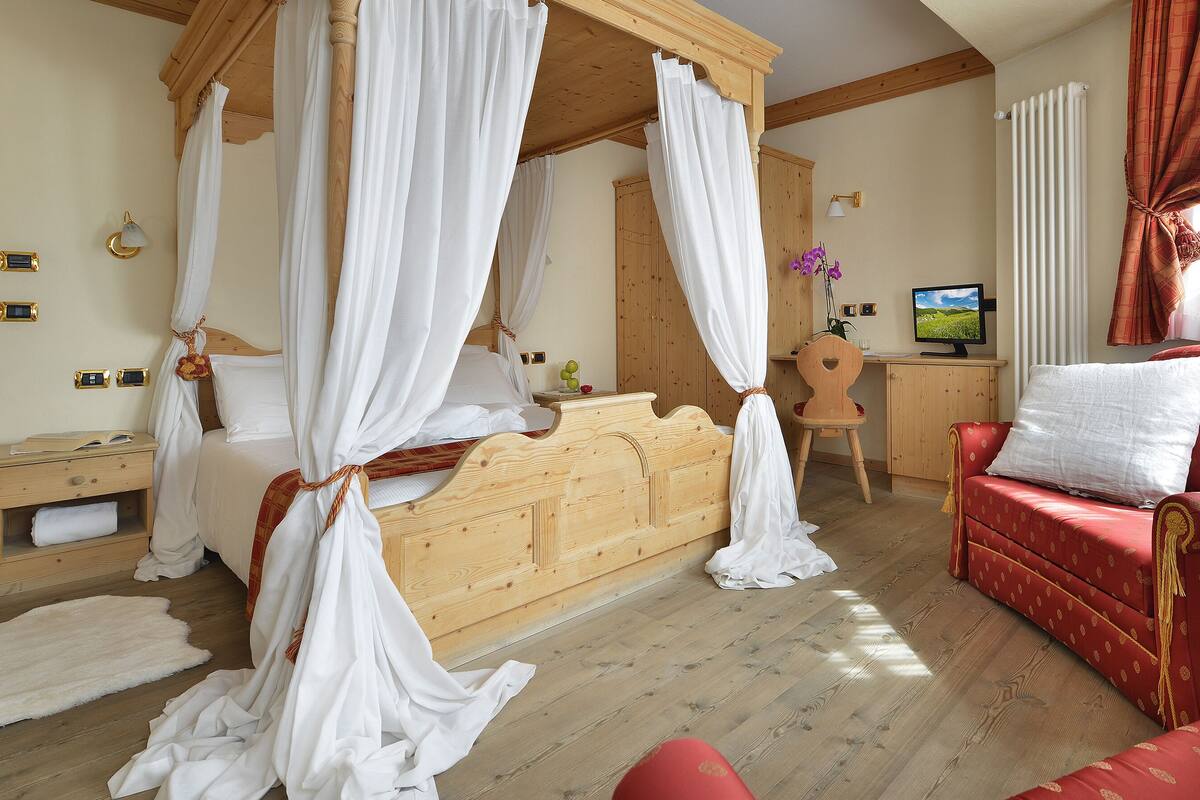 A bedroom with a four-poster bed, a red sofa, a wooden desk, and a television.