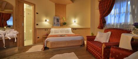 A wooden-floored bedroom with a bed, a red upholstered sofa, and a large window with curtains.