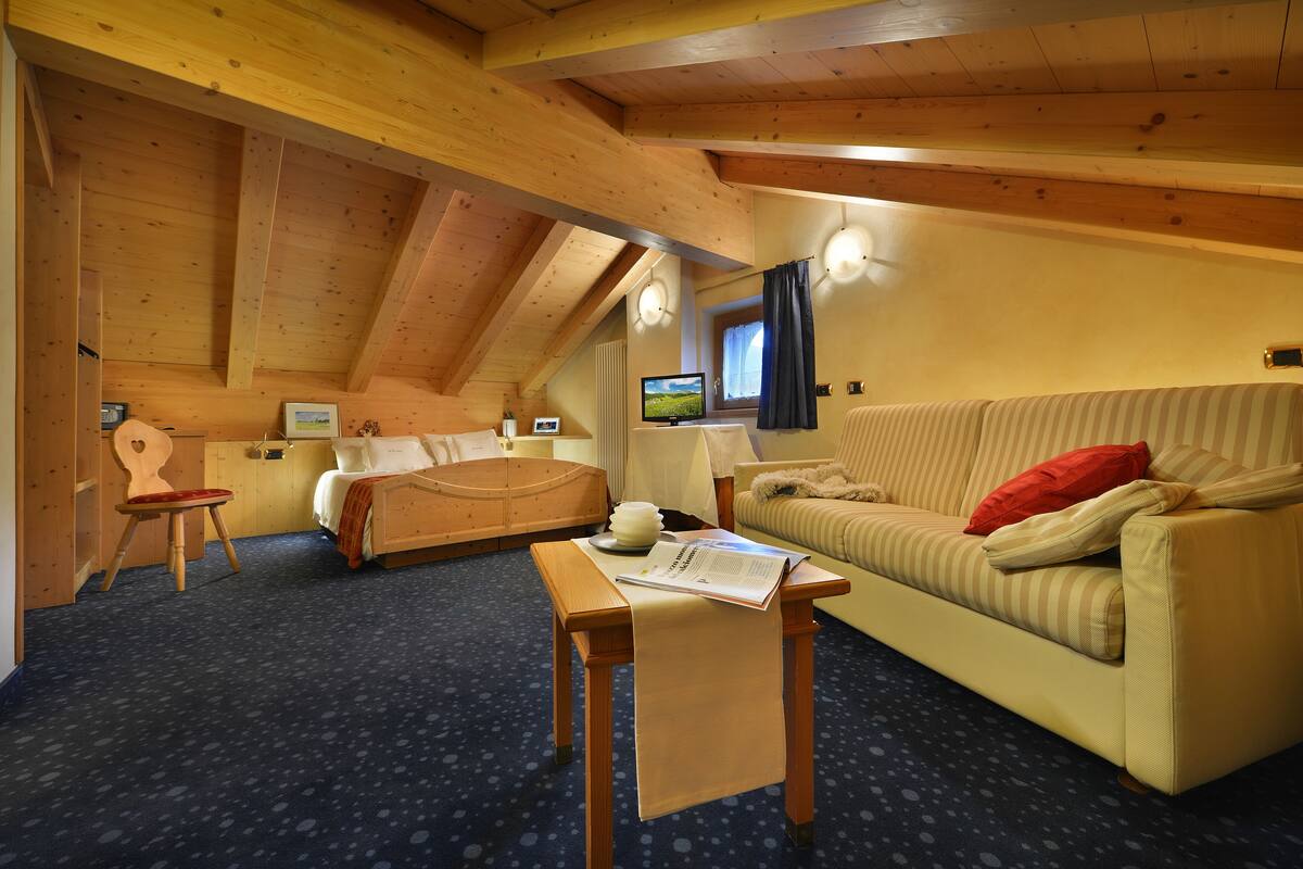 A cozy room with a wooden ceiling, a sofa, a chair, a small table, and a television.