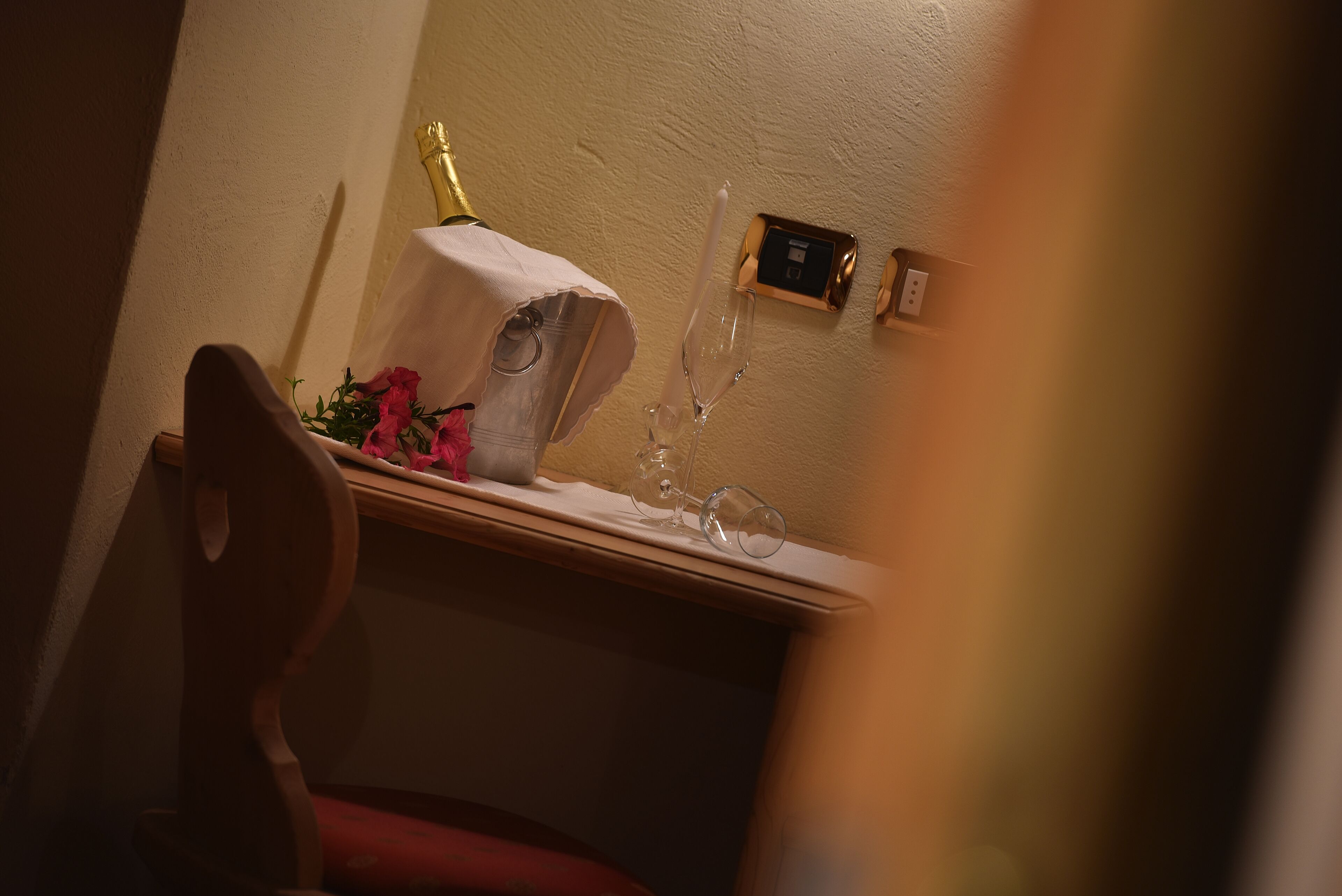 Un coin de pièce avec une chaise en bois, une petite table sur laquelle se trouvent une bouteille, un verre et un arrangement floral.