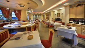 Un restaurante con mesas redondas, asientos acolchados en rojo y una vitrina de vinos.