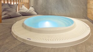 Jacuzzi redondo con borde texturizado, frente a una pared de azulejos grises.