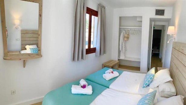 A double bed with teal bedding, a wooden headboard, and a mirror on the wall. - Sa Torre (Capdepera)