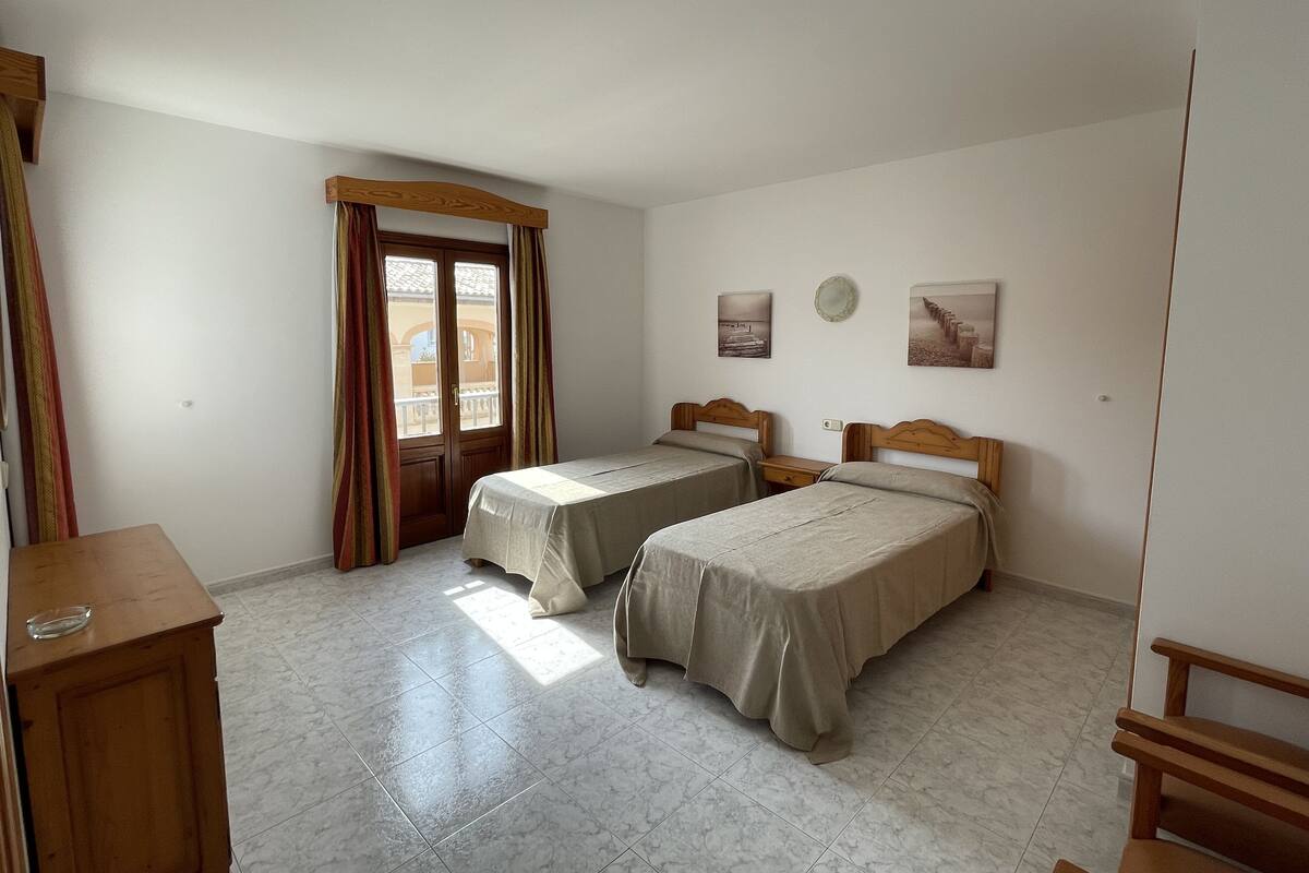 A room with two beds, a wooden wardrobe, a small table, and a door with curtains.
