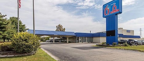 A 6.6 Extended Sky motel with a blue roof, an American flag, and a parking lot.