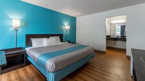 A hotel room with a large bed, two bedside lamps, a nightstand, a desk, a chair, a mirror, and a view of the bathroom. - Concorde Inn Suites Pekin (Pekin)