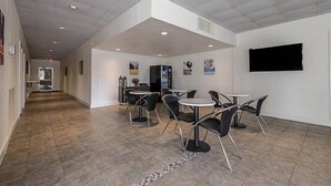 A modern indoor space with a long corridor leading to a seating area with tables and chairs. - Concorde Inn Suites Pekin (Pekin)