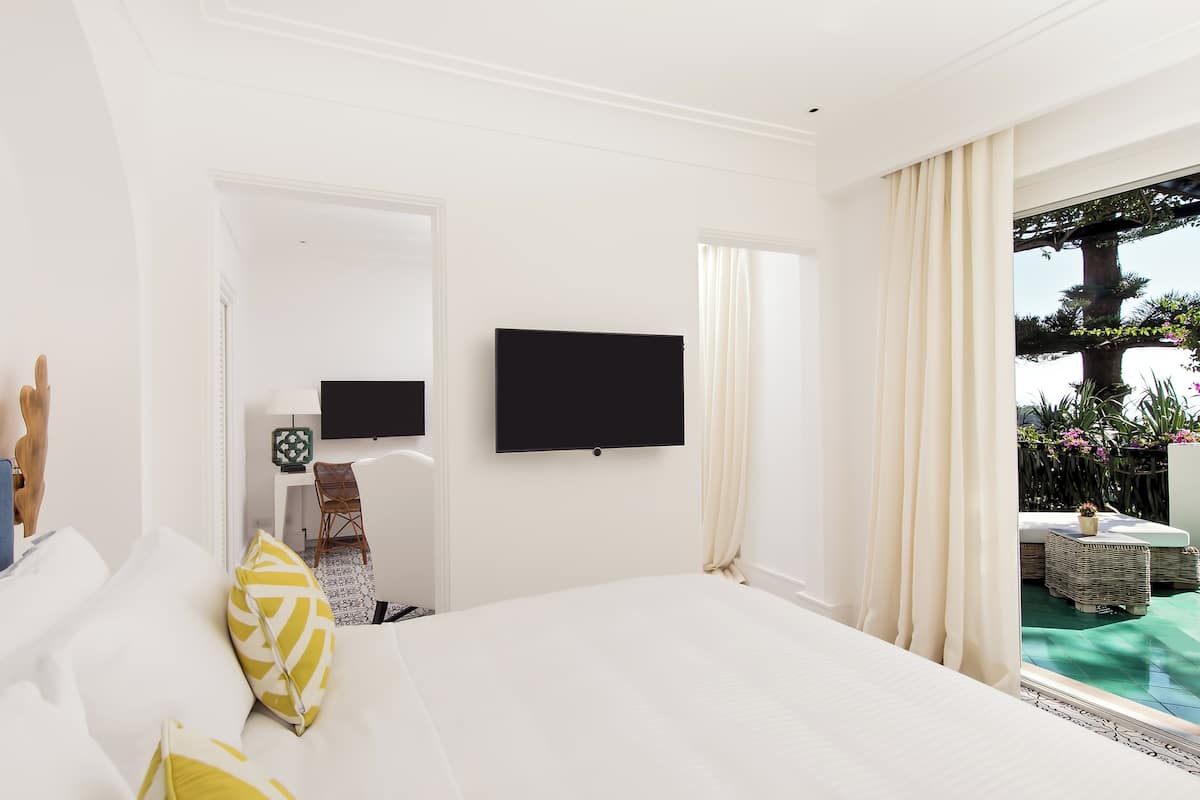 A hotel room with a large bed, a flat-screen TV, a desk with a chair, and a view of a pool and outdoor area.