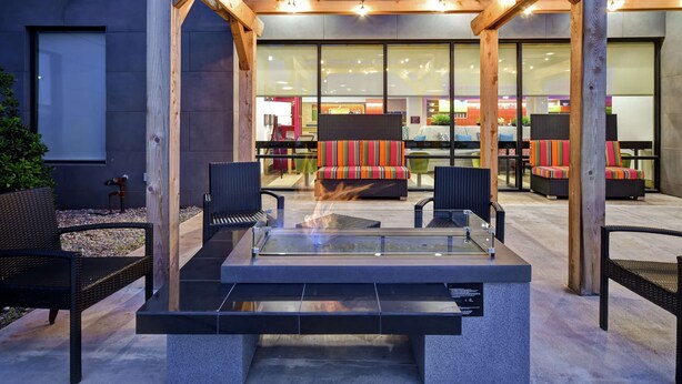 An outdoor seating area with a glass-top fire pit, wooden pergola, and modern furniture. - Home2 Suites by Hilton Oklahoma City Airport (Oklahoma City)