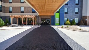 A modern building entrance with a covered walkway, outdoor seating, and a mix of brick and glass facades. - Home2 Suites by Hilton Oklahoma City Airport (Oklahoma City)