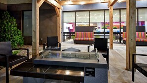 An outdoor seating area with wicker furniture and a glass-top table, surrounded by wooden beams and large windows. - Home2 Suites by Hilton Oklahoma City Airport (Oklahoma City)