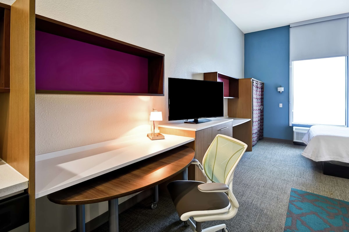 Ein Hotelzimmer mit Schreibtisch, Stuhl, Fernseher, Bett und Fenster.