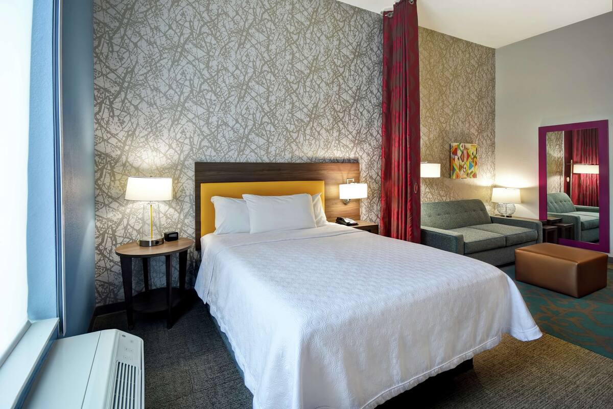 Ein Hotelzimmer mit einem großen Bett, zwei Nachttischen mit Lampen, einem Sofa, einem kleinen Tisch und einem Spiegel.