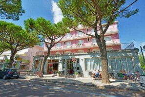 A pink building with a balcony, a covered entrance, and a seating area with people. - Tokio (Venezia)