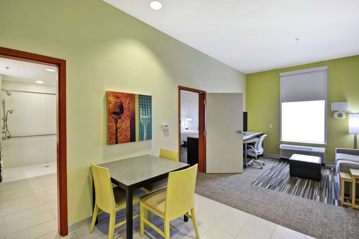 A modern hotel room with a dining area, a shower, and a large window.