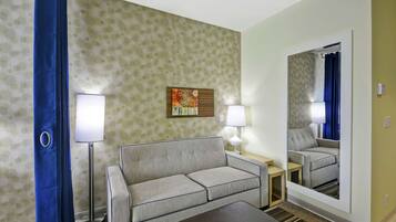 A hotel room with a sofa, a small table, a lamp, a mirror, and a blue curtain.