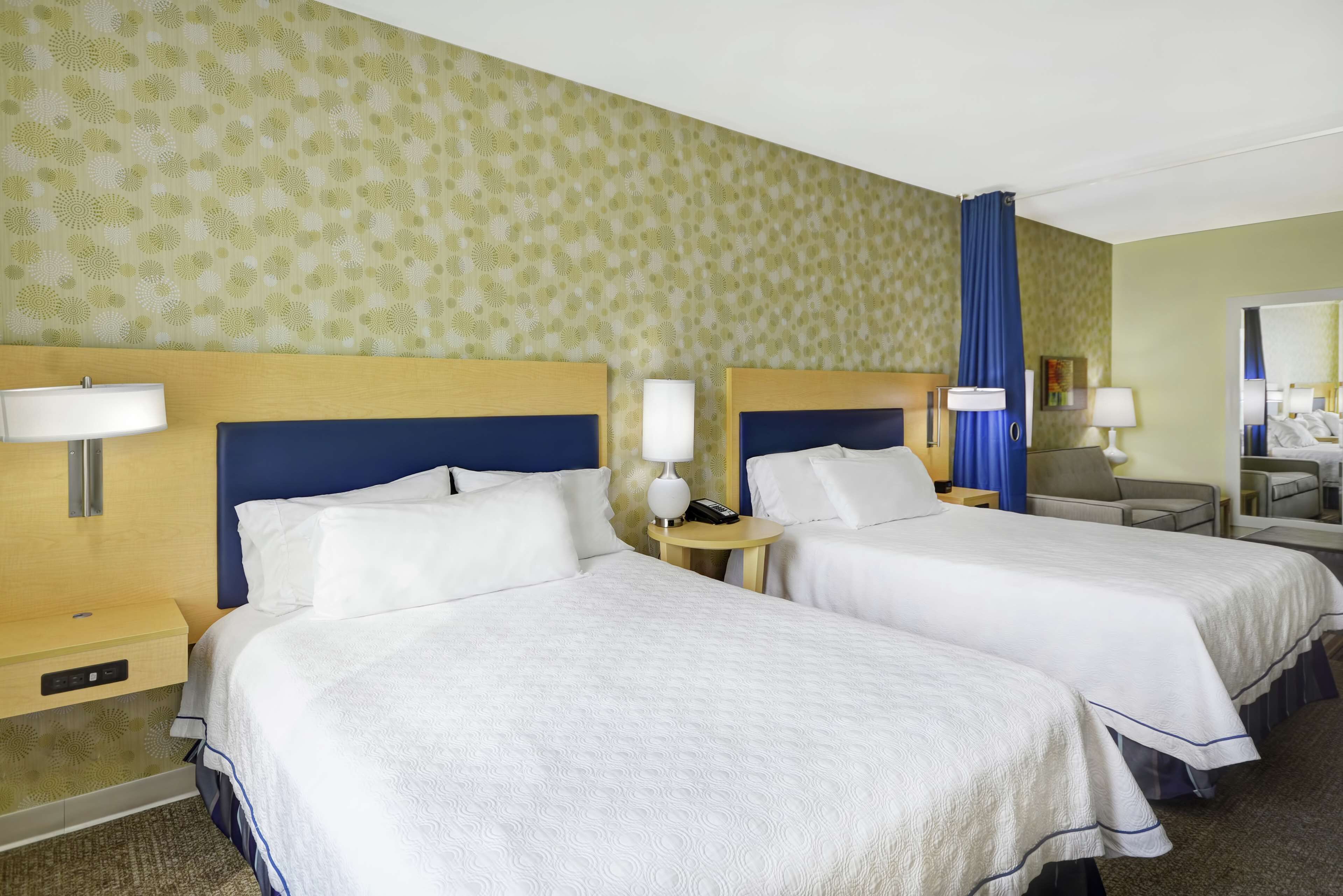 A hotel room with two beds, each with a headboard, bedside tables, lamps, and a mirror.
