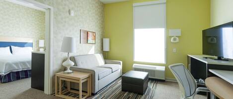 A hotel room with a bed, a sofa, a desk, a chair, and a TV.