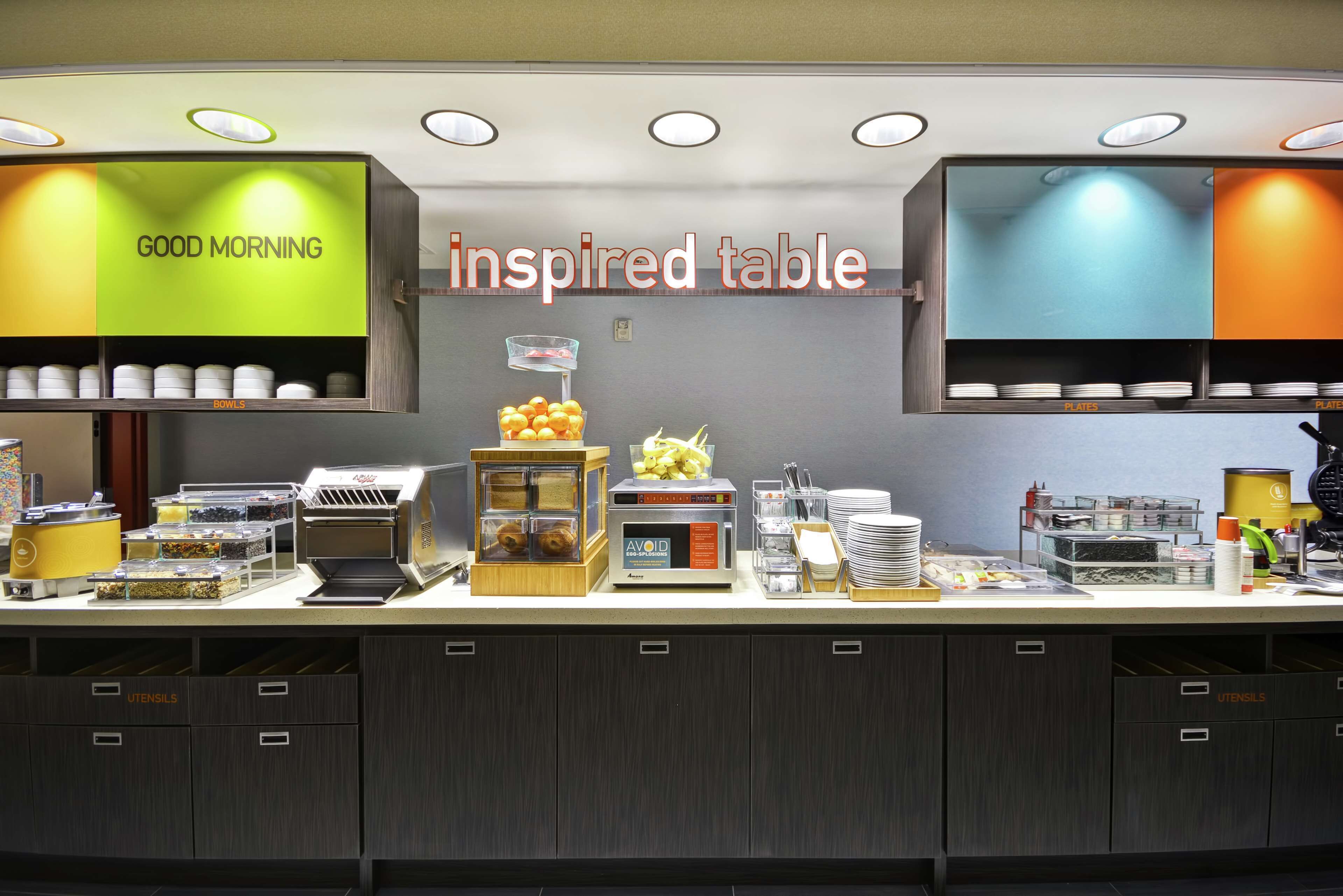 Una barra de desayuno con un letrero que dice 'Good Morning', una máquina de café de autoservicio y diversas opciones para el desayuno.