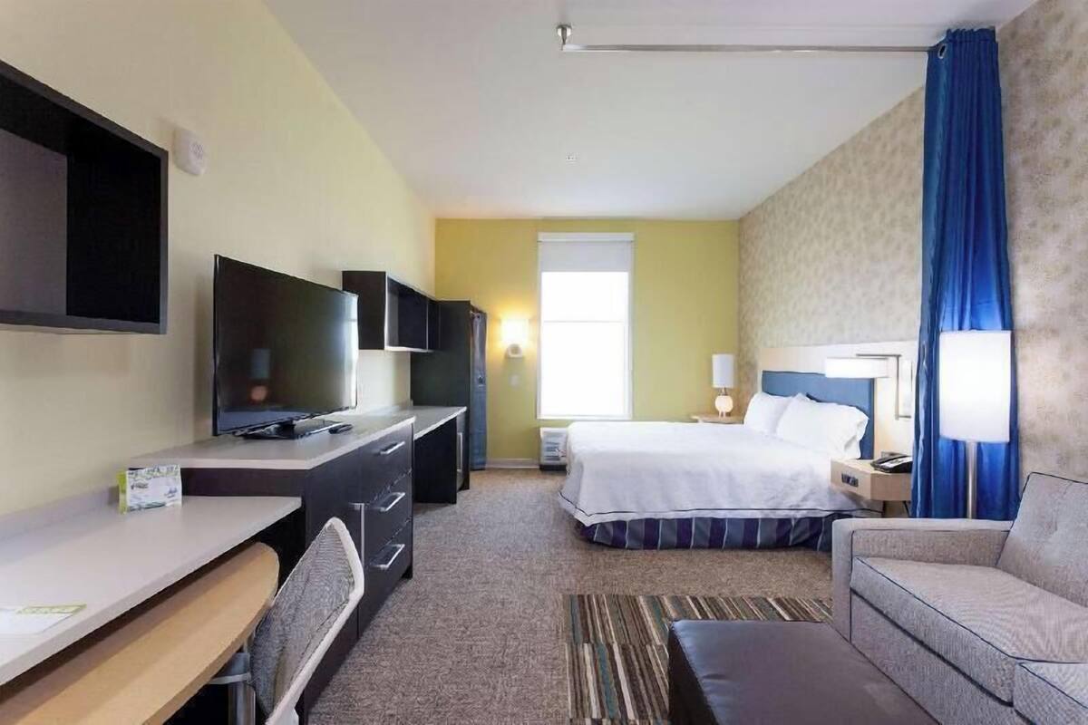 A hotel room with a bed, a desk, a TV, a chair, a sofa, and a window.