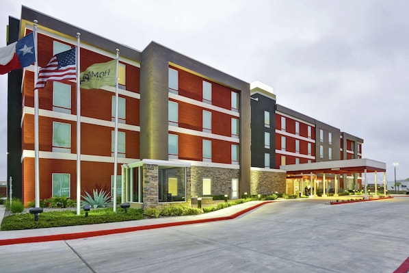 Un hotel moderno con fachada roja y marrón, múltiples ventanales y un área de entrada cubierta.