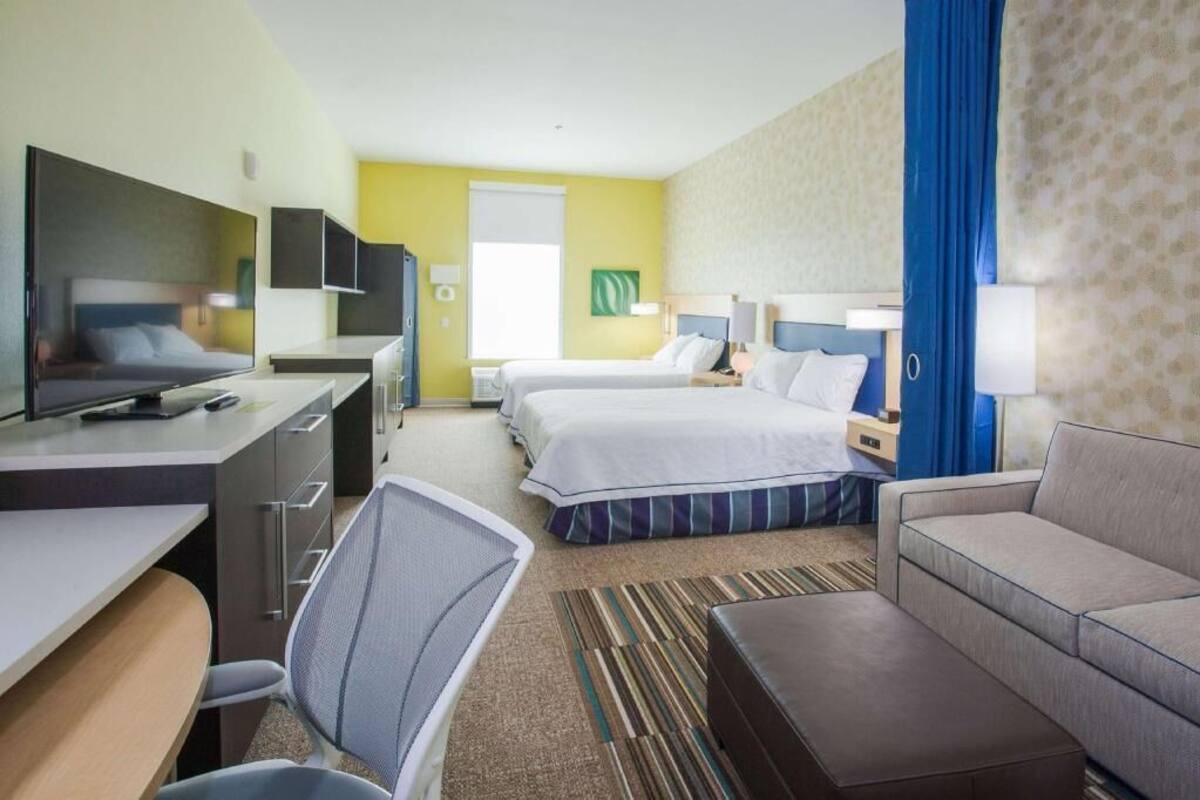 A hotel room with a desk, two beds, a sofa, a TV, and a window.