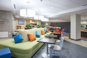 Eine moderne Hotelhalle mit einem grünen Sofa, mehreren Tischen und Sesseln, einem Fernseher und einer Rezeption.