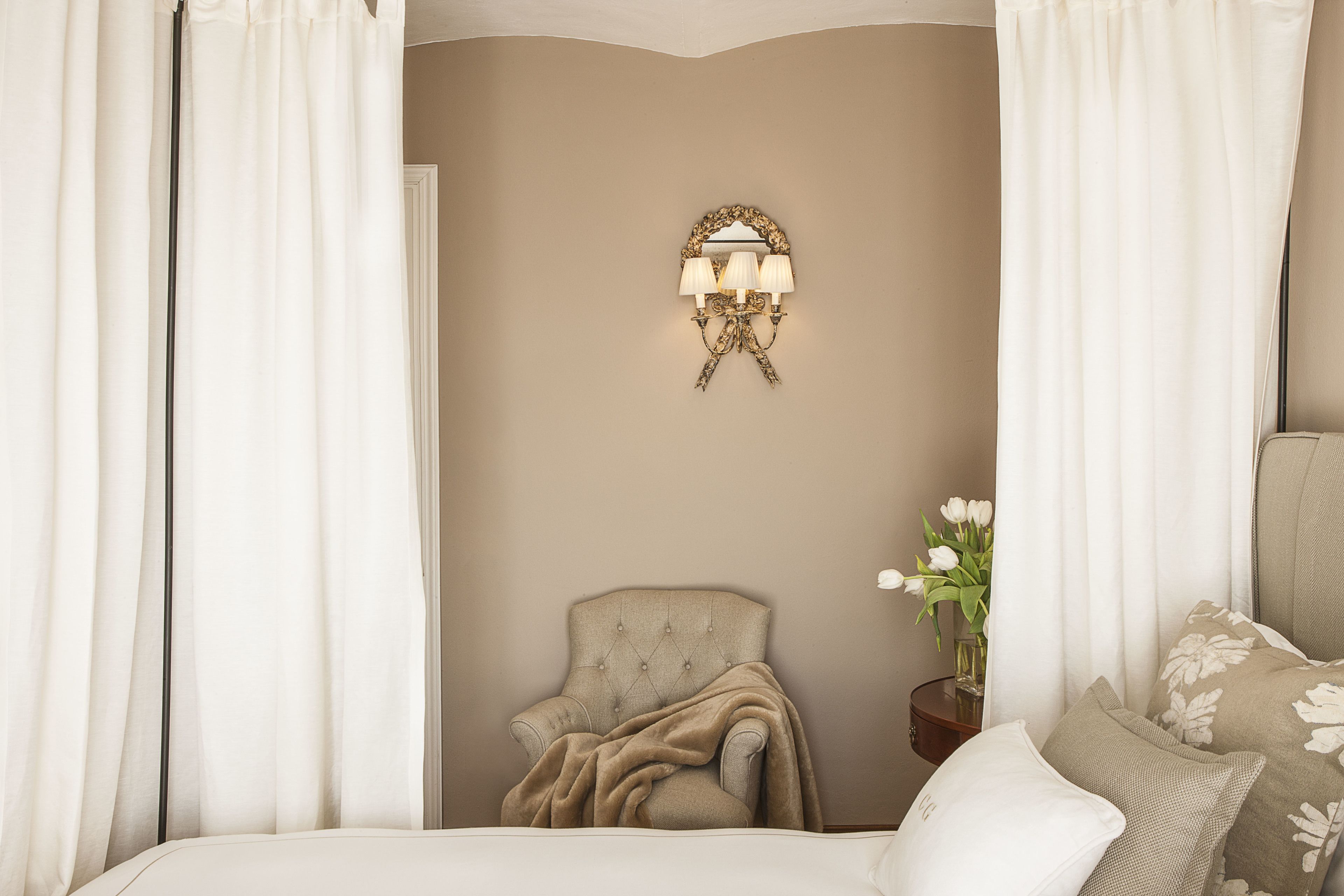 Une chambre à coucher avec un lit, une chaise, une table de chevet, une lampe et un miroir.